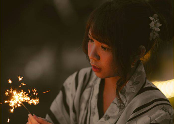 A girl in a kimono looking at a lit sparkler.